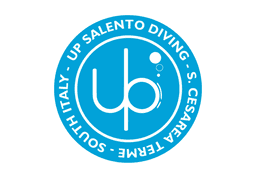 Logo di Up Salento Diving | Shop al centro stilizzati in bianco ci sono una U e una P che vanno a formare la faccia di un subacqueo. Il logo è circolare con sfondo celeste e scritte in bianco.